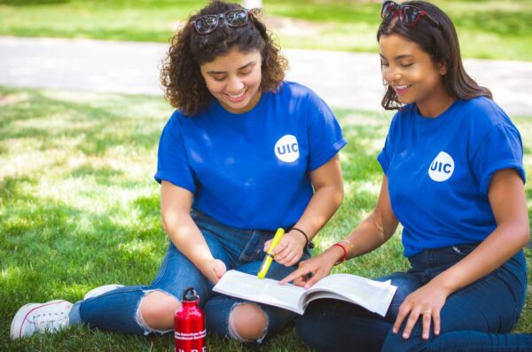 two students sitting outside on the grass chatting and studying together